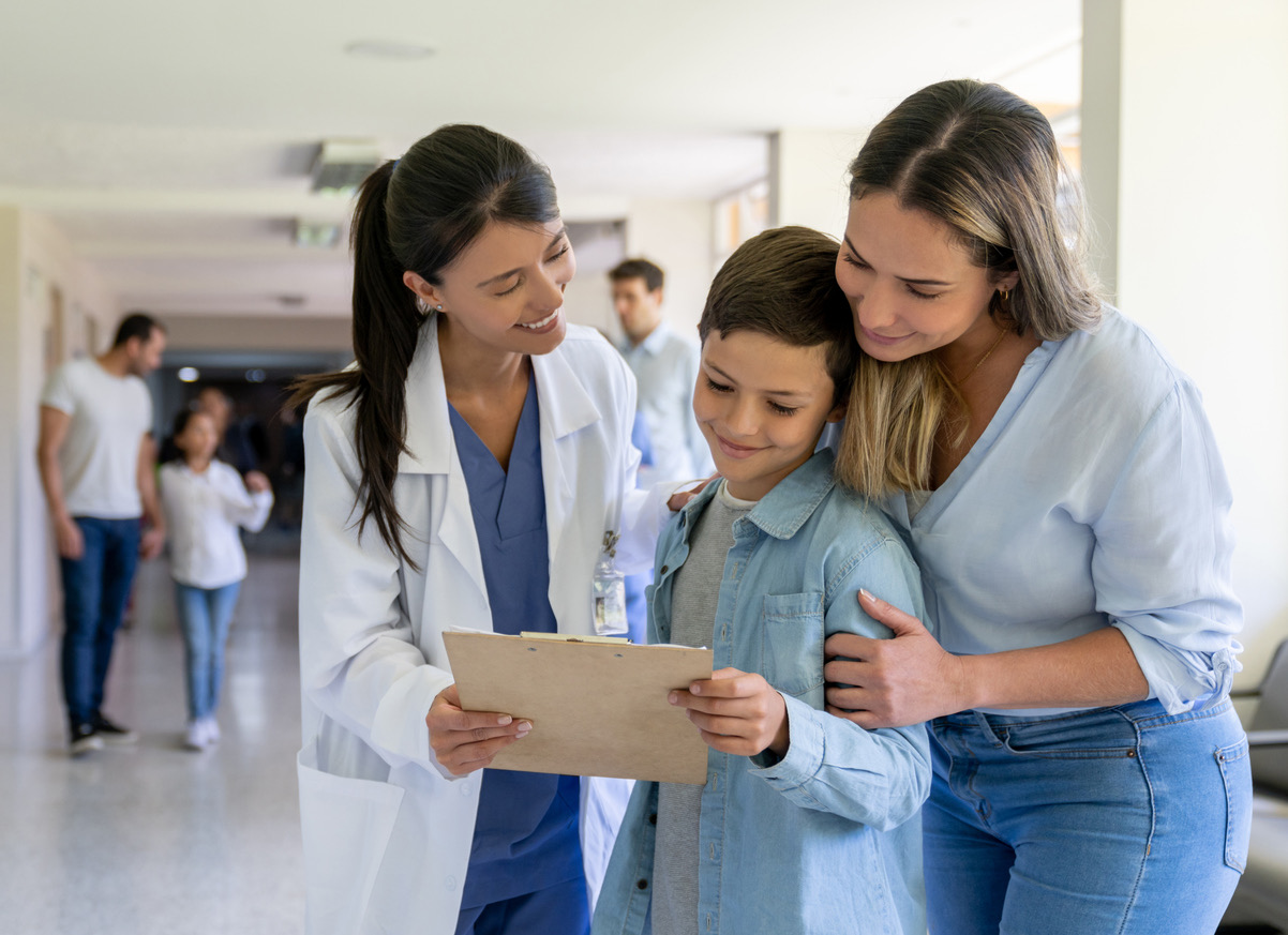 A pediatrician showing a clipboard to a mother and her son during a family visit